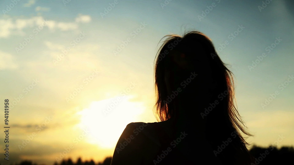 A silhouette of a woman on a sunset turns her head A silhouette of a woman on a sunset turns her head