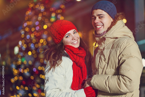 Christmas and people concept - young winter couple over christmas tree outdoor