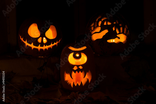 Photo composition from three pumpkins for Halloween. Jack, a Cyclops and hands of pumpkin against autumn leaves and candles