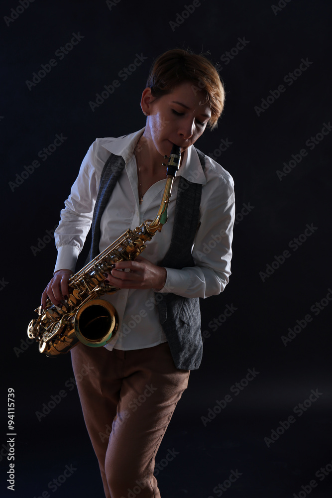 Naklejka premium Attractive woman plays saxophone on black background