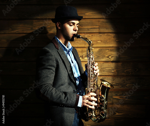 Elegant saxophonist plays jazz on wooden background