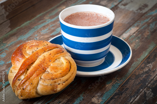 Swedish cinnamon berry bun served on a rustic wooden table with a cup of freshly brewed coffee in a blue and white striped cup and saucer. Coffee and a bun is a tradition in Sweden known as fika. photo