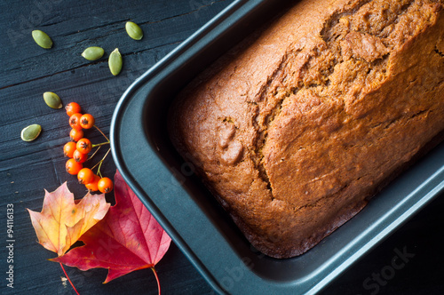 Freshly baked pumpkin bread cake in a baking tin. Served with a scattering of pumpkin seeds and some autumn fall leaves and berries. photo