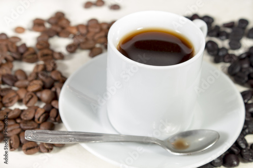 Coffee cup and teaspoon over a saucer, beside natural roasted and torrefacto coffee beans