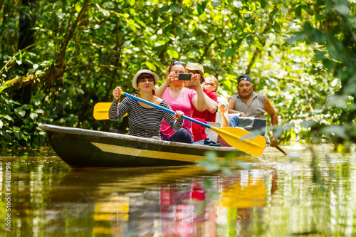 A group of tourists on a boat in the Amazon jungle, fishing and exploring the river while surrounded by lush wildlife and a vibrant community. © Ammit