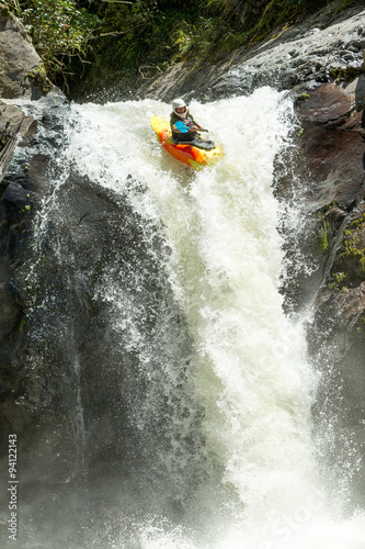 A thrilling image of kayakers navigating through extreme whitewater rapids on a raft in Ecuador, with a stunning waterfall in the background.