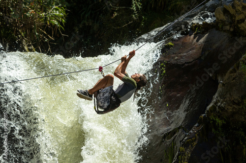 A thrilling zipline adventure in Ecuador, soaring over lush mountains and a rushing river with a breathtaking waterfall in the background.