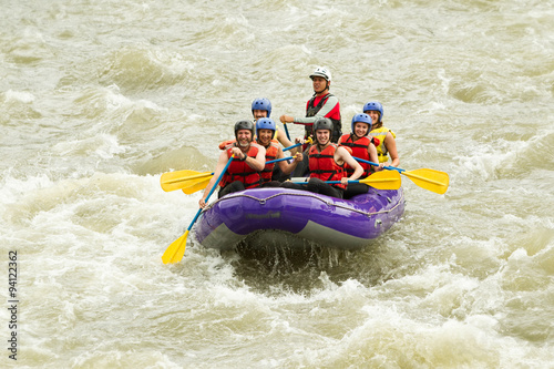 A group of seniors wearing helmets and rowing a raft down a river in South America, enjoying a fun family holiday on the water.