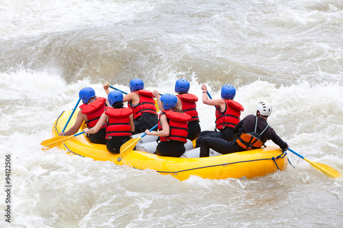 A diverse group of women paddle a white-water raft together, demonstrating teamwork as they navigate through thrilling rapids on a river.