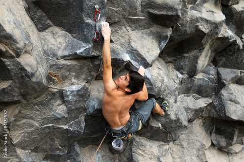 A male climber scaling a steep rock face, navigating dangerous terrain with skill and determination, feeling free in his element.