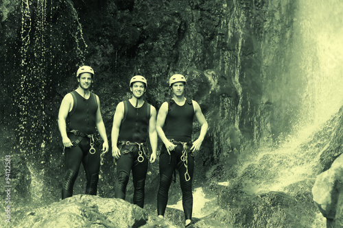 Three young men dressed in sport suits posing against a breathtaking waterfall,showcasing their athletic prowess and love for adventure.
