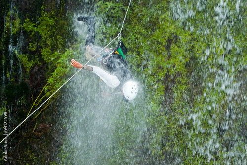 A daring canyoning enthusiast rappelling down a steep cliff face, pushing the limits of extreme sports despite the risk of accident. photo