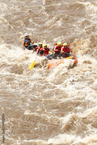 A group of people in survival gear are doing exercises on a raft in the middle of a rushing river.