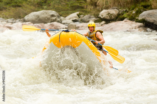 A team of adventurers navigating through white water rapids on a raft, battling the rushing river with skill and teamwork.