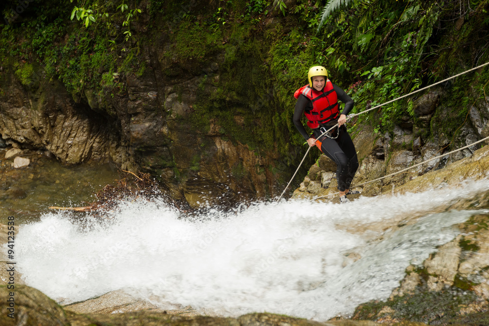 Obraz premium A group of women racing down a waterfall while rappelling during a canyoning descent, each person securely attached to a rope.