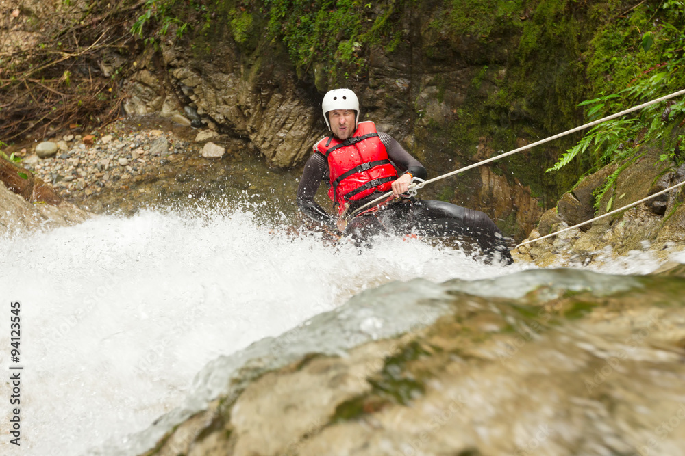 A daring human in climbing equipment rappels down a waterfall in a canyon, experiencing an adrenaline rush while canyoning. A daring human in climbing equipment rappels down a waterfall in a canyon, experiencing an adrenaline rush while canyoning.