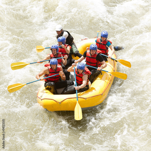 A team of athletes rowing a white raft through intense whitewater rapids in a thrilling competition on the river.