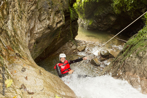 A man in a wetsuit navigating through an extreme canyoning adventure, rappelling down waterfalls for a thrilling recreational experience.