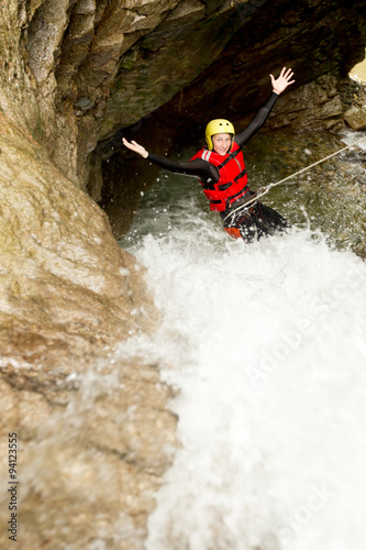 Experience the thrill of adventure as you witness an adult woman clad in waterproof gear descending a majestic waterfall. © Ammit