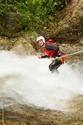 Adult man wearing waterproof equipment descending a breathtaking waterfall,showcasing his adventurous spirit and love for extreme sports.