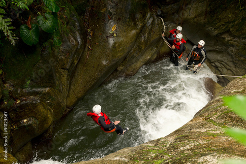 A man, an outdoor instructor and climber, stands at the edge of a canyon overlooking a rushing river below.
