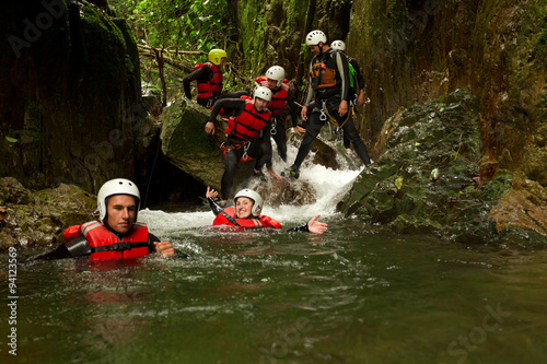 A group of adventurous individuals in harnesses navigating a canyon in the lush rainforest of Baños, Ecuador, engaging in extreme canyoning activity.
