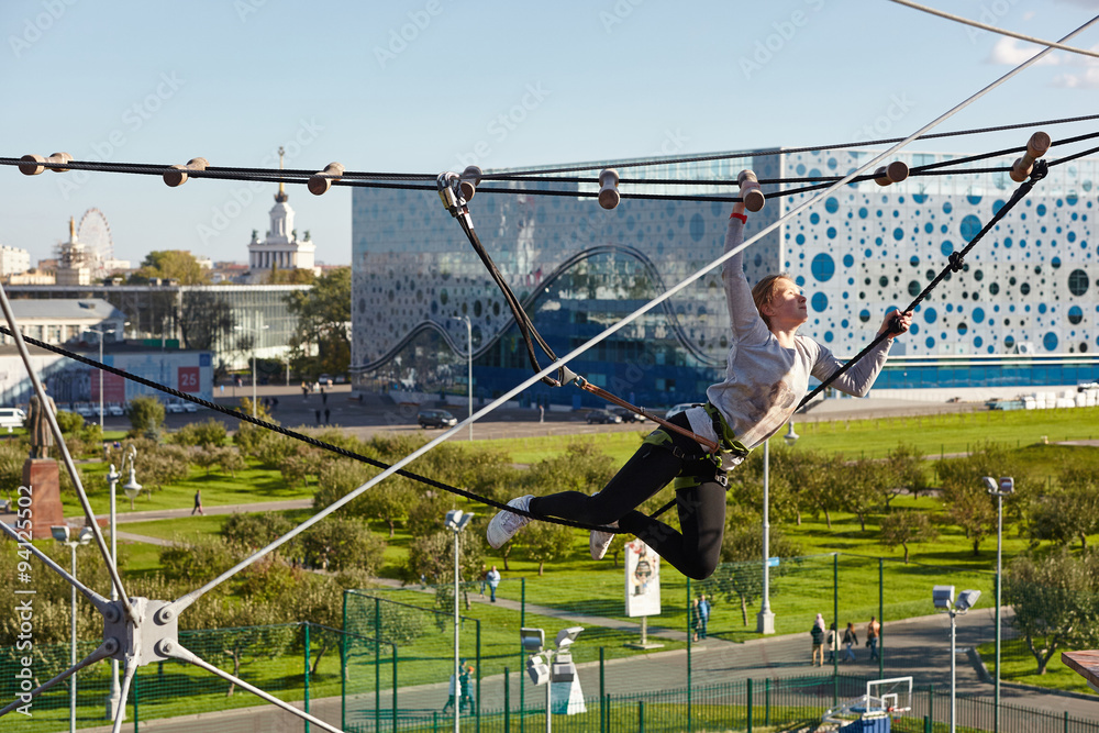 Naklejka premium Girl athlete runs an obstacle course in climbing park