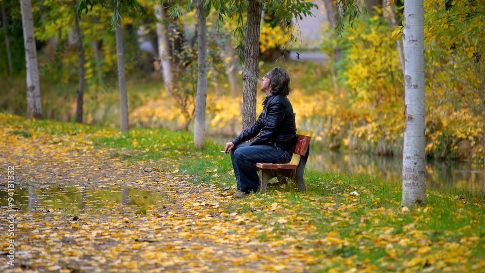 man smoking on a bench in autumn man smoking on a bench in autumn