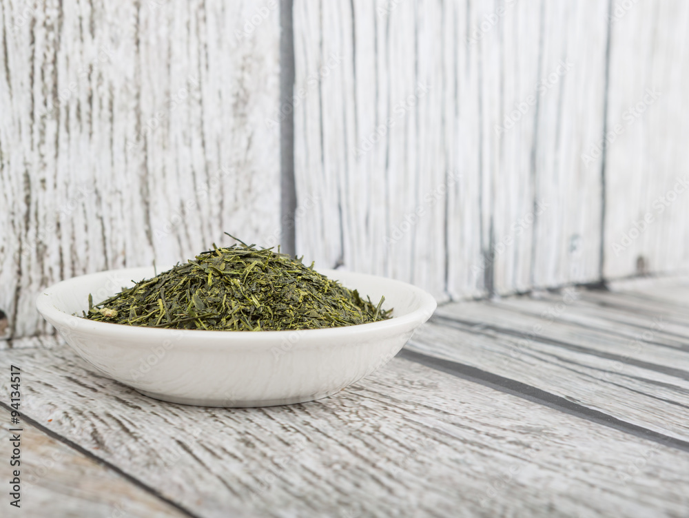 Dried green tea leaves in white bowl over wooden background Dried green tea leaves in white bowl over wooden background