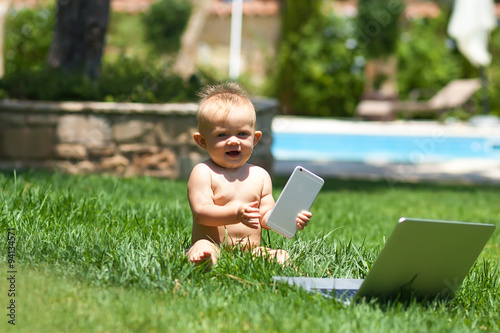 Cute baby playing with laptop outdoors on green grass