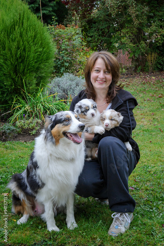 Fototapeta Dog breeder with Australian Shepherd adult female dog and her puppies in arms