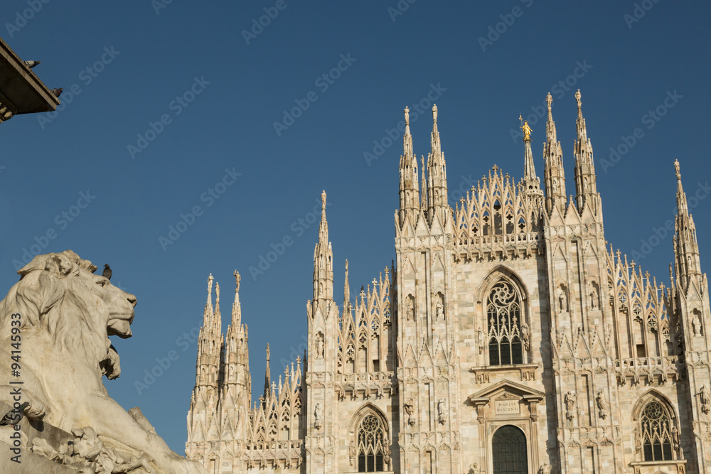 lion statue and the gothic Duomo or Milan Cathedral dedicated to St. Mary of the Nativity, Milan, Italy