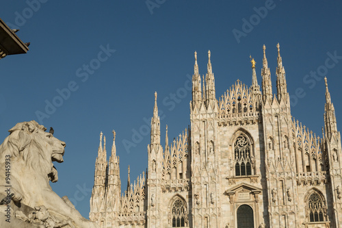 lion statue and the gothic Duomo or Milan Cathedral dedicated to St. Mary of the Nativity, Milan, Italy