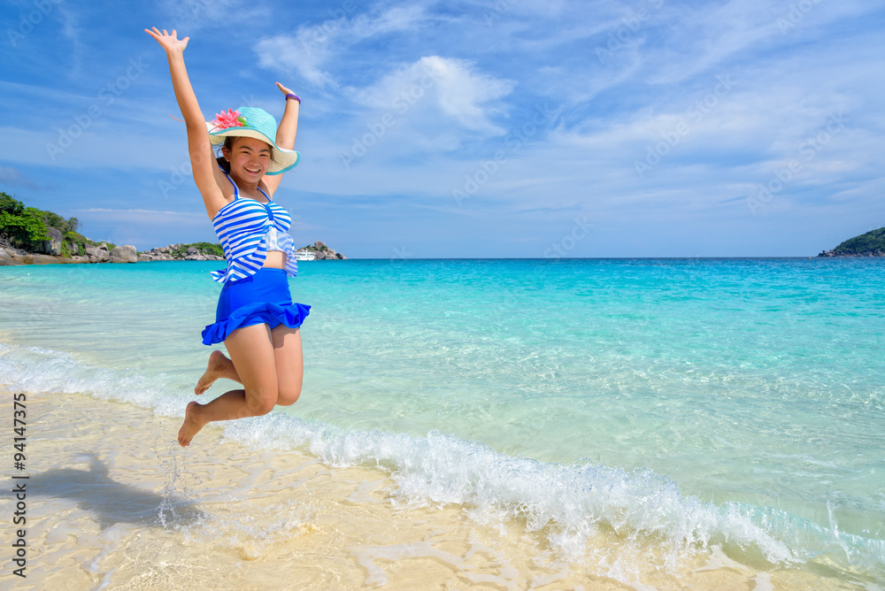Tourist girl in a blue white striped swimsuit jumping with happy on the beautiful beach and sea during summer at Koh Miang Island, Mu Ko Similan National Park, Phang Nga province, Thailand