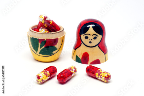 Red granule pills and babushka nesting dolls on white background