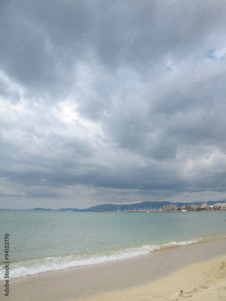 Sandy beach with turquoise water and dark skies in Mallorca, Balearic islands, Spain in August.