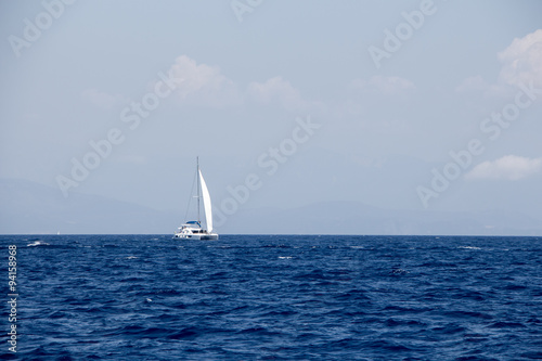 Seascape sailing boat, distant mountains and fluffy clouds