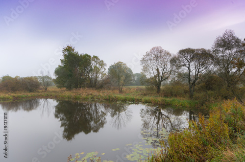 Early morning view of calm lake surrounded by trees © tomeyk