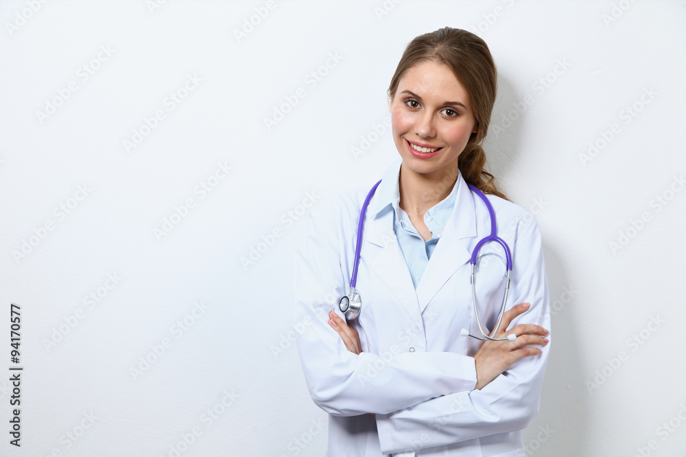 Friendly smiling young female doctor, standing near wall Friendly smiling young female doctor, standing near wall