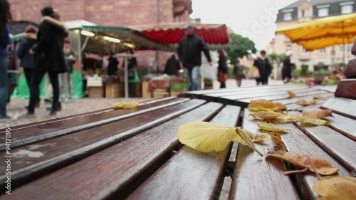 Green market at central city square (marktplatz) in Ettlingen - Baden Wurttemberg, Germany; few autumn leaves at park bench with blurry people in background;