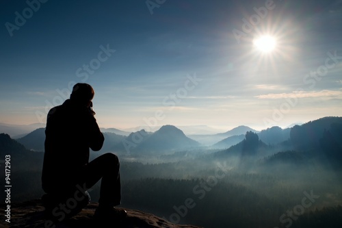 Professional photographer takes photos with mirror camera on peak of rock. Dreamy landscape, orange Sun at horizon