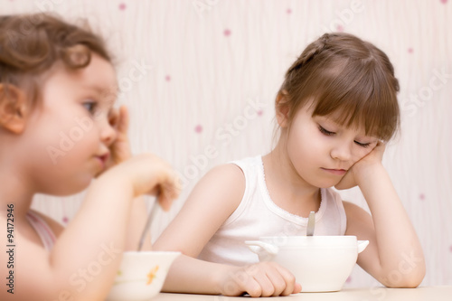 Two pretty little girls eating without appetite