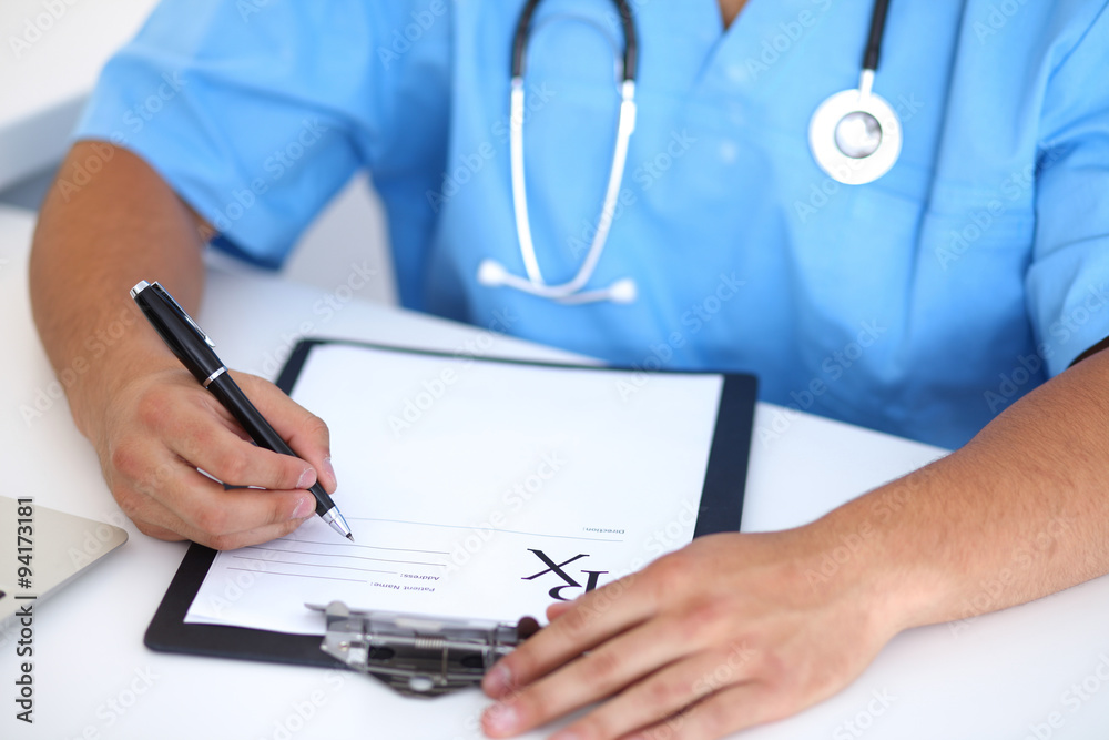 Portrait of unknown male surgeon doctor holding his stethoscope and filling up medical prescription Portrait of unknown male surgeon doctor holding his stethoscope and filling up medical prescription