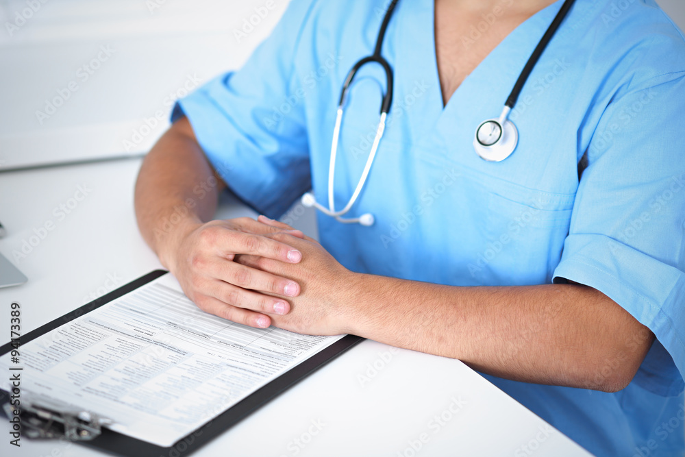 Portrait of unknown male surgeon doctor sitting at the table in hospital office, stethoscope Portrait of unknown male surgeon doctor sitting at the table in hospital office, stethoscope