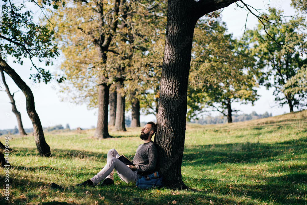 Handsome Young bearded student man hipster reading book in park on a summers sunny day Handsome Young bearded student man hipster reading book in park on a summers sunny day