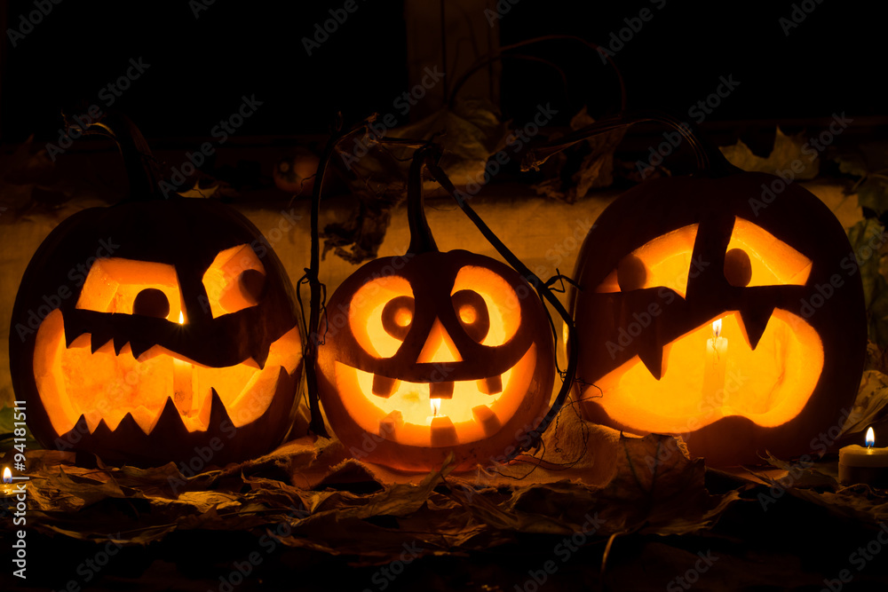 Fototapeta premium Photo composition from three pumpkins on Halloween. Embittered, mad and afraid of some pumpkin against an old window, leaves and candles.