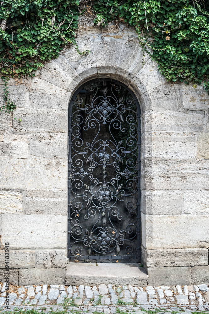 Fototapeta premium Old medieval black metal door with cerved bar and light stone