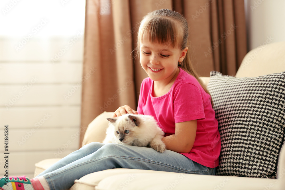 Little cute girl playing with kitten on sofa at home Little cute girl playing with kitten on sofa at home