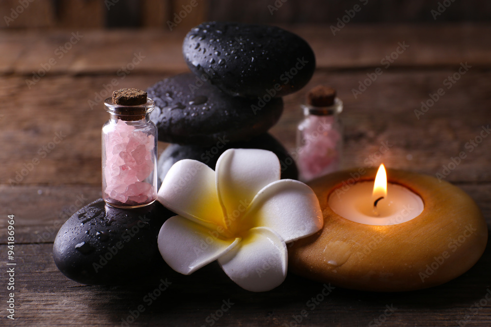 Relaxing set of fragipani flower, pebbles and alight candle on wooden background Relaxing set of fragipani flower, pebbles and alight candle on wooden background