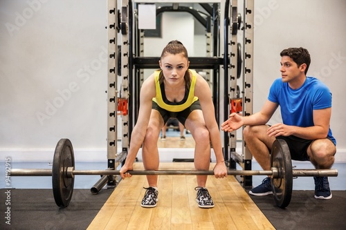Woman lifting barbell with trainer spotting her